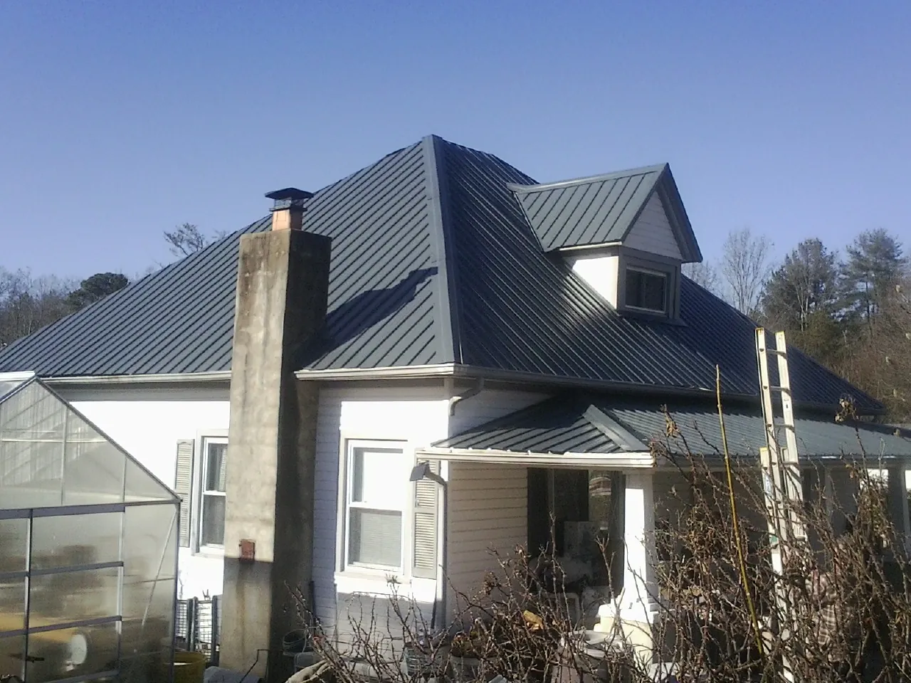 Dark blue standing seam metal roof on a white farmhouse with dormer — Slate & Tile Roof Repair by Roofing Brothers in Belfield
