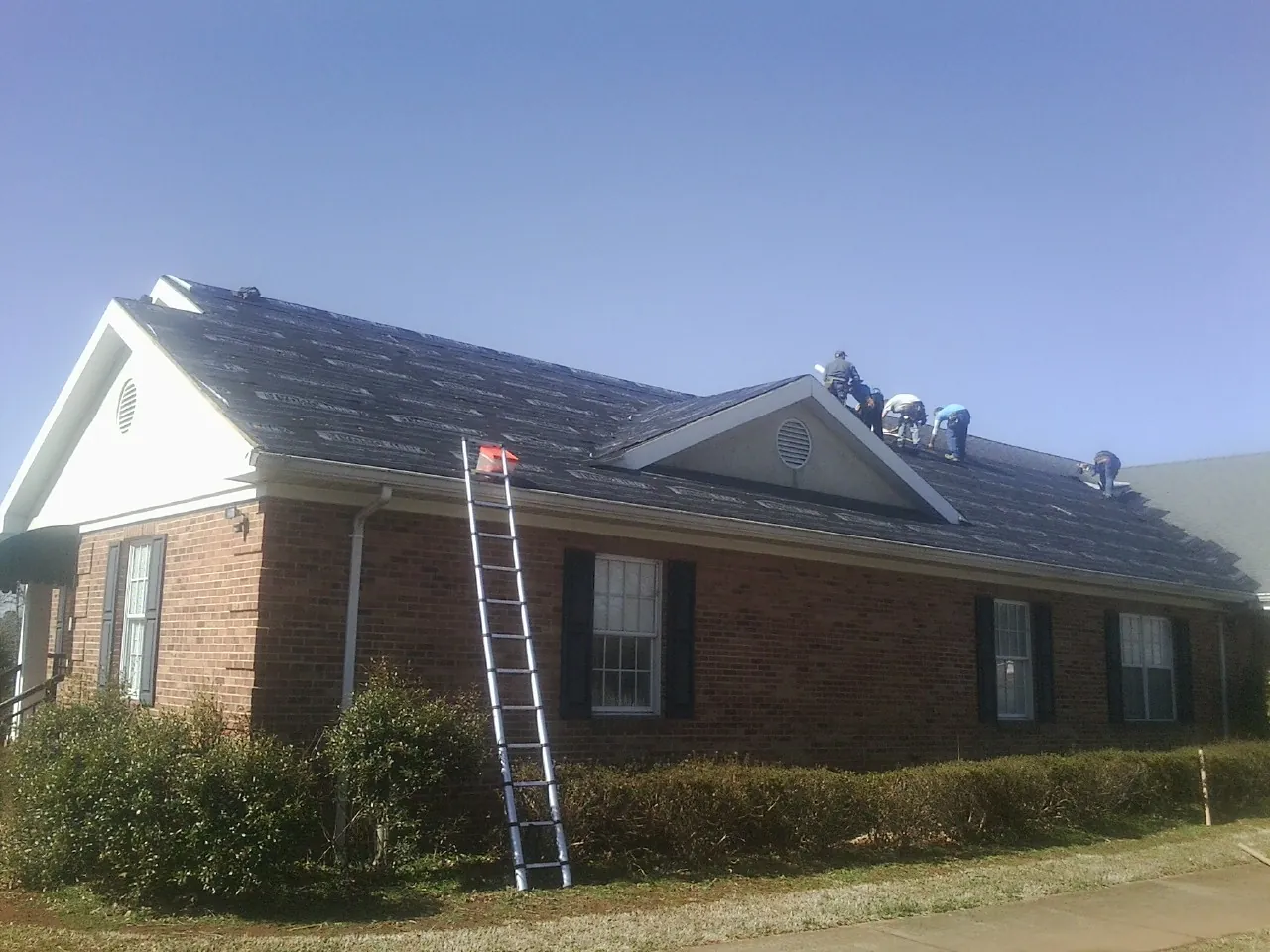Crew tearing shingles off a brick ranch roof with a ladder set — Emergency Roof Repair work by our crew in Belfield