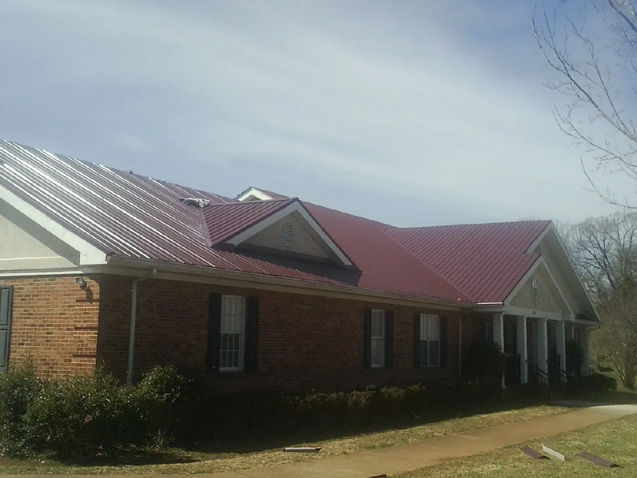 Red metal roof with gabled entries on a long brick building, from a Hail Damage Roof Repair job in Belfield