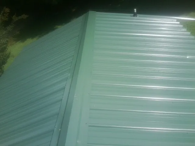 New green metal panels meeting at the ridge of a roof — Flat Roof Repair work by our crew in Belfield