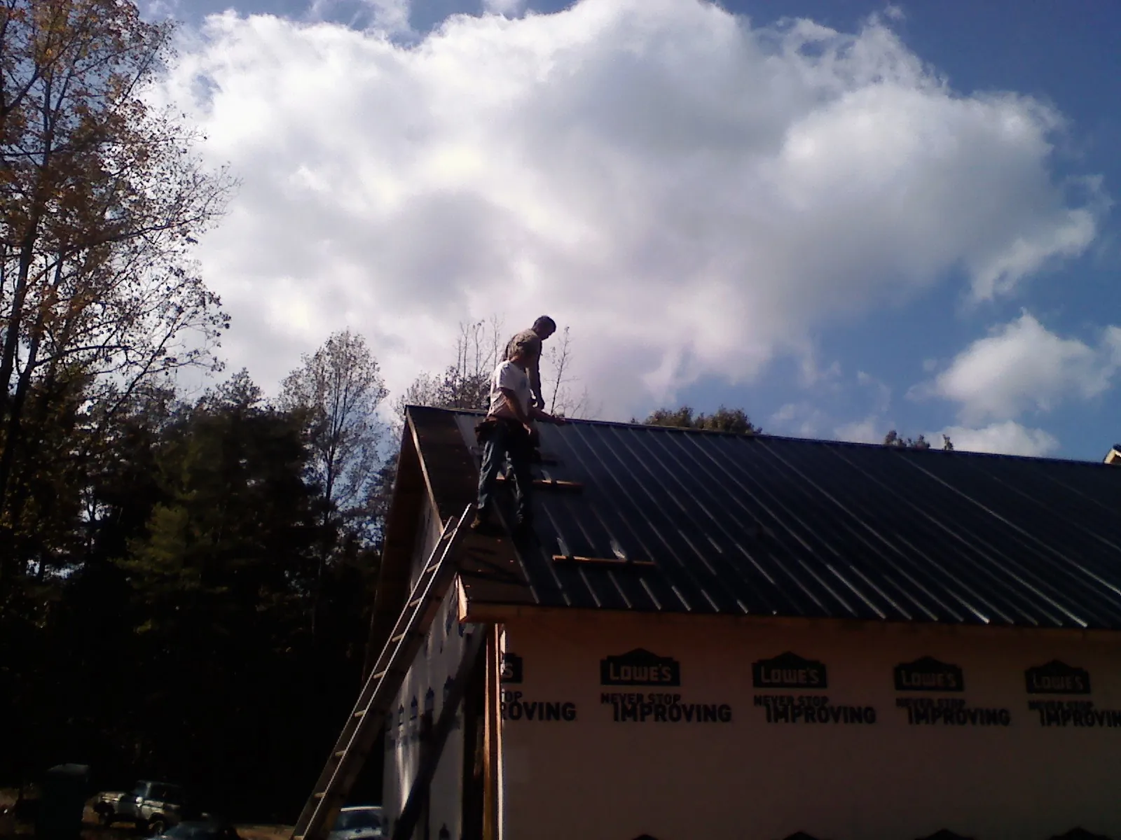 Roofer fastening dark metal panels high against a cloudy sky, from a Roof Inspection job in Belfield