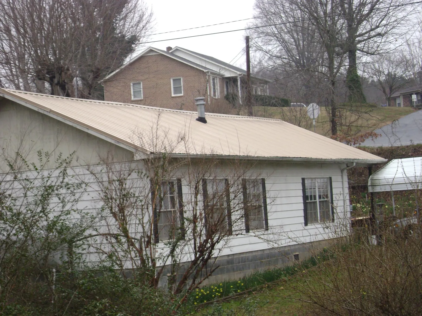 Tan metal roof on a white sided house set into a hillside — Commercial Roofing by Roofing Brothers in Belfield