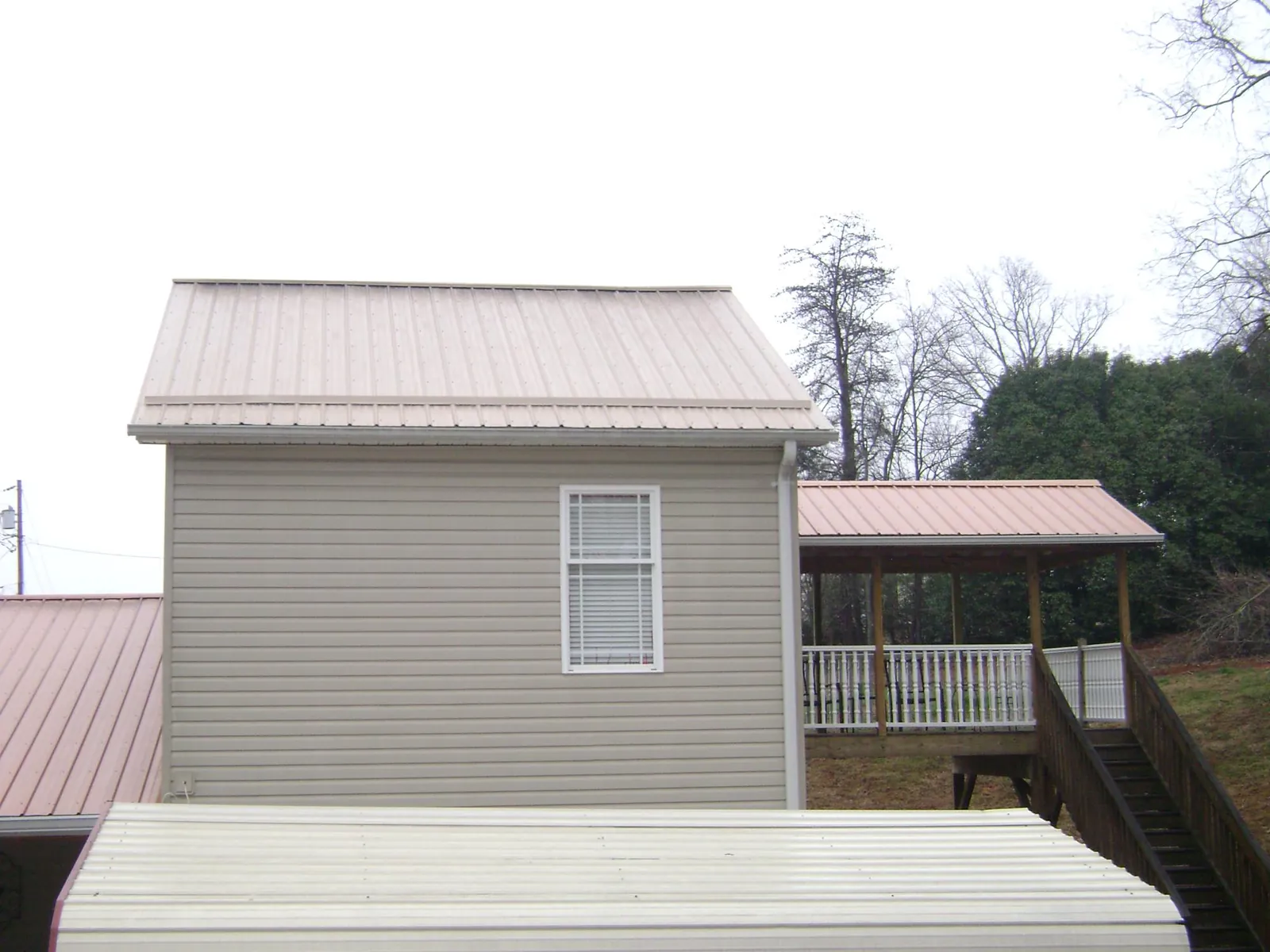Tan metal roofs on a two story addition and attached porch, from a Roof Replacement job in Belfield